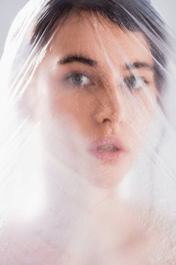 Polietilen kaplı esmer kadın gri ekoloji konseptine izole edilmiş kameraya bakıyor.