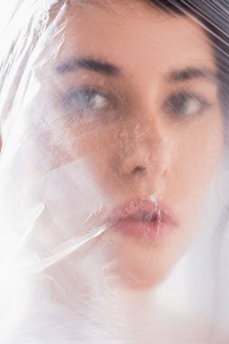 Polietilen kaplı esmer kadının yakın çekimleri kameraya, ekoloji konseptine bakıyor.