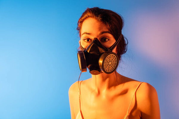 brunette model in gas mask looking at camera on blue