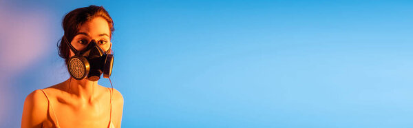 panoramic concept of brunette woman in gas mask looking at camera on blue