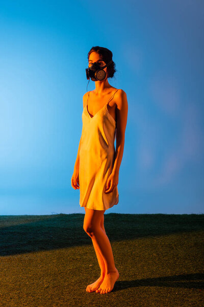 young and barefoot woman in gas mask standing on blue