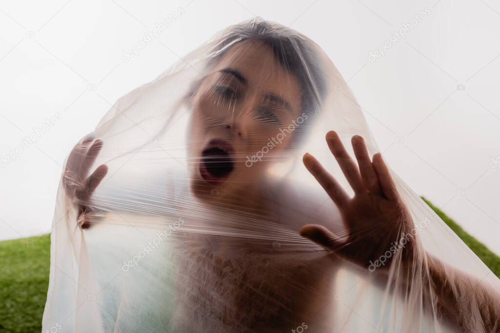 brunette woman screaming through polyethylene on white, ecology concept