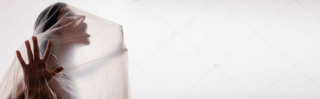 panoramic shot of brunette woman screaming through polyethylene isolated on white, ecology concept