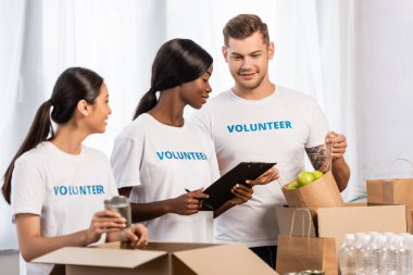 Bağış merkezinde paketleri tutarken panoya bakan çok kültürlü gönüllülerin seçici odak noktası 