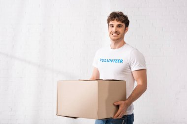 Gönüllü yardım merkezinde paketi tutarken kameraya bakıyor 