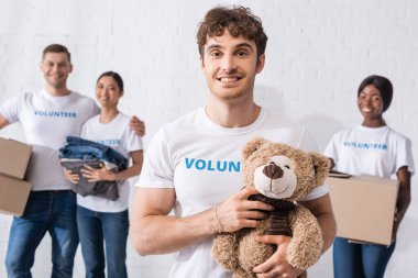 Yardım merkezinde paketleri olan çok kültürlü gönüllülerin yanında yumuşak oyuncakları tutan adamın seçici odak noktası. 