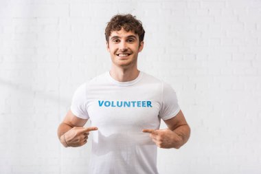 Young man pointing with fingers at volunteer lettering on t-shirt  clipart