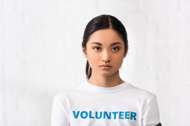 Asian woman with volunteer lettering on t-shirt looking at camera in charity center  clipart