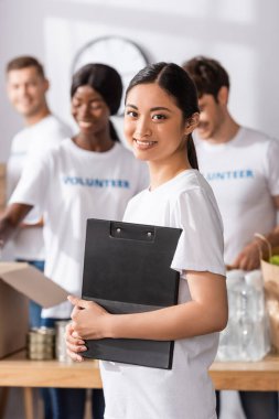 Selective focus of asian volunteer holding clipboard in charity center  clipart