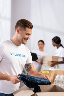 Gönüllülerin, hayır merkezindeki karton kutunun yanında kot pantolon tutması seçici bir odak noktası. 