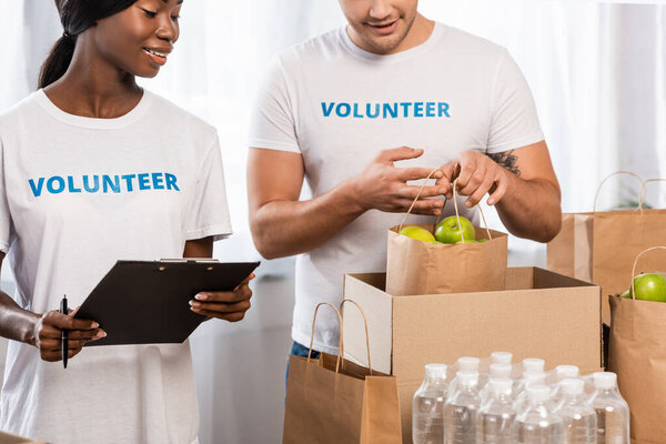 Selective focus of volunteer holding package with apples near african american woman with clipboard 