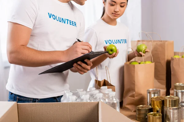 Selective Focus Man Writing Clipboard Asian Volunteer Holding Apples Packages — Stock Photo, Image