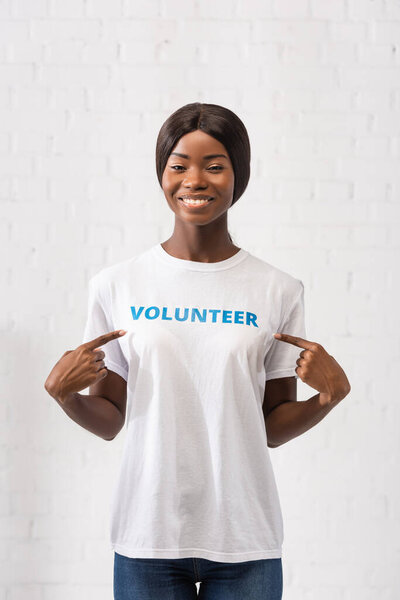 Young african american volunteer pointing at lettering on t-shirt in charity center 