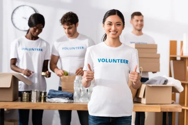 Enfoque Selectivo Voluntarios Asiáticos Mostrando Pulgares Hacia Arriba Cerca Donaciones — Foto de Stock