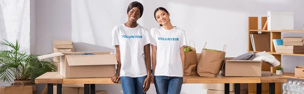 Imagen Horizontal Voluntarios Multiétnicos Mirando Cámara Cerca Cajas Cartón Mesa —  Fotos de Stock