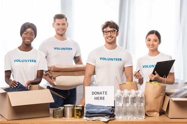 Voluntarios Multiétnicos Con Portapapeles Ropa Pie Cerca Tarjeta Con Donar —  Fotos de Stock