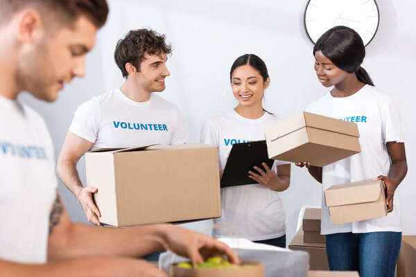 Selective focus of multiethnic volunteers holding clipboard and boxes in charity center 