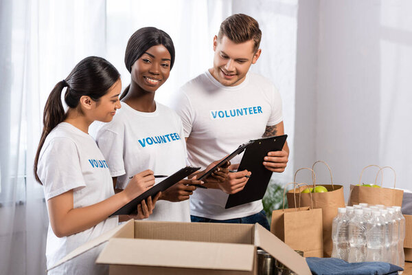 Селективный фокус мультиэтнических волонтеров с планшетами, стоящими рядом с пожертвованиями в благотворительном центре 