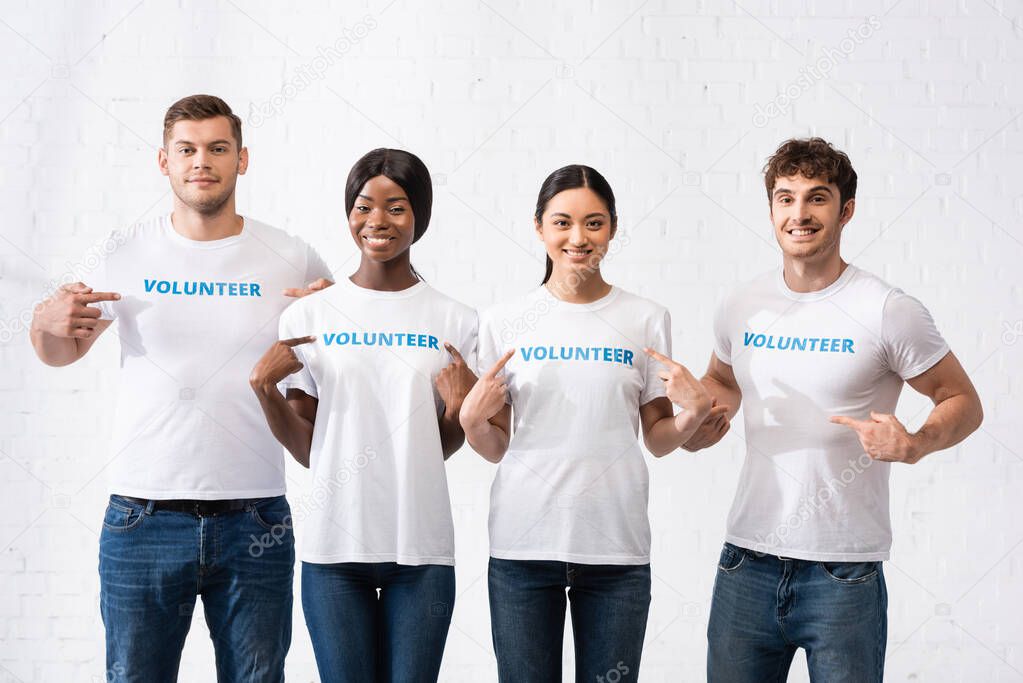 Multiethnic volunteers pointing with fingers at lettering on t-shirts 