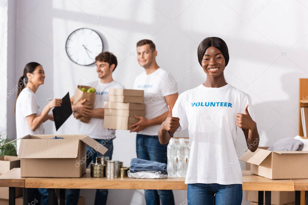 Selective focus of african american volunteer showing like gesture near donations and multiethnic people in charity center 