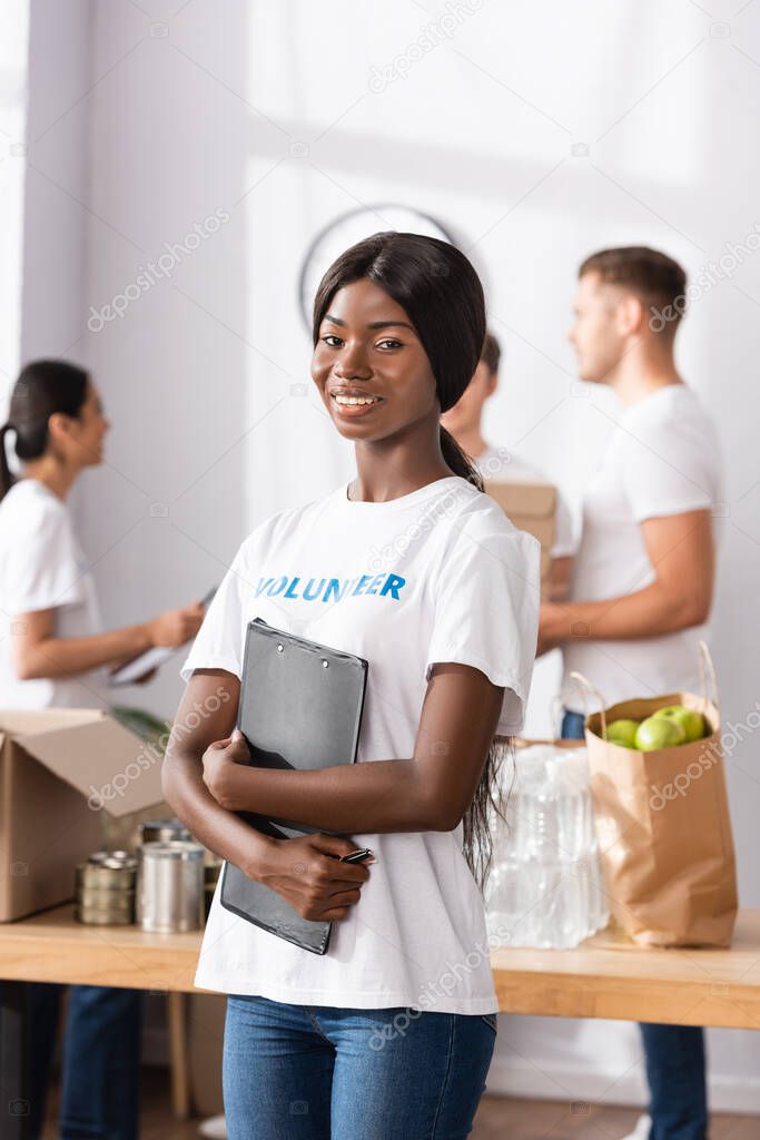 Selective focus of african american woman holding clipboard near donations and people in charity center 