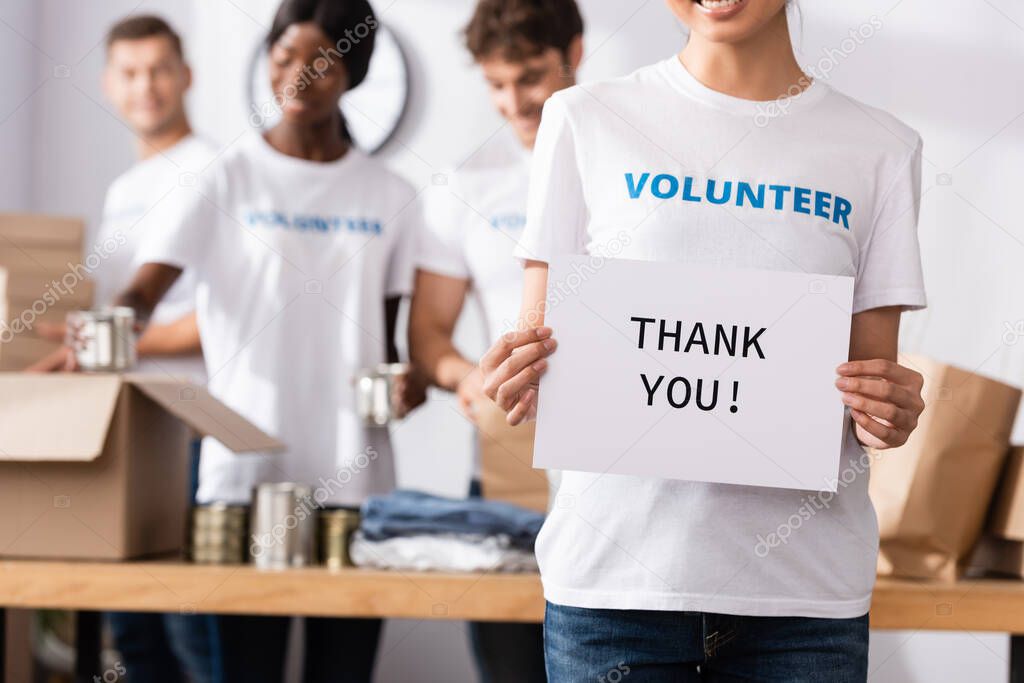 Selective focus of volunteer holding card with thank you lettering near donations and multiethnic people
