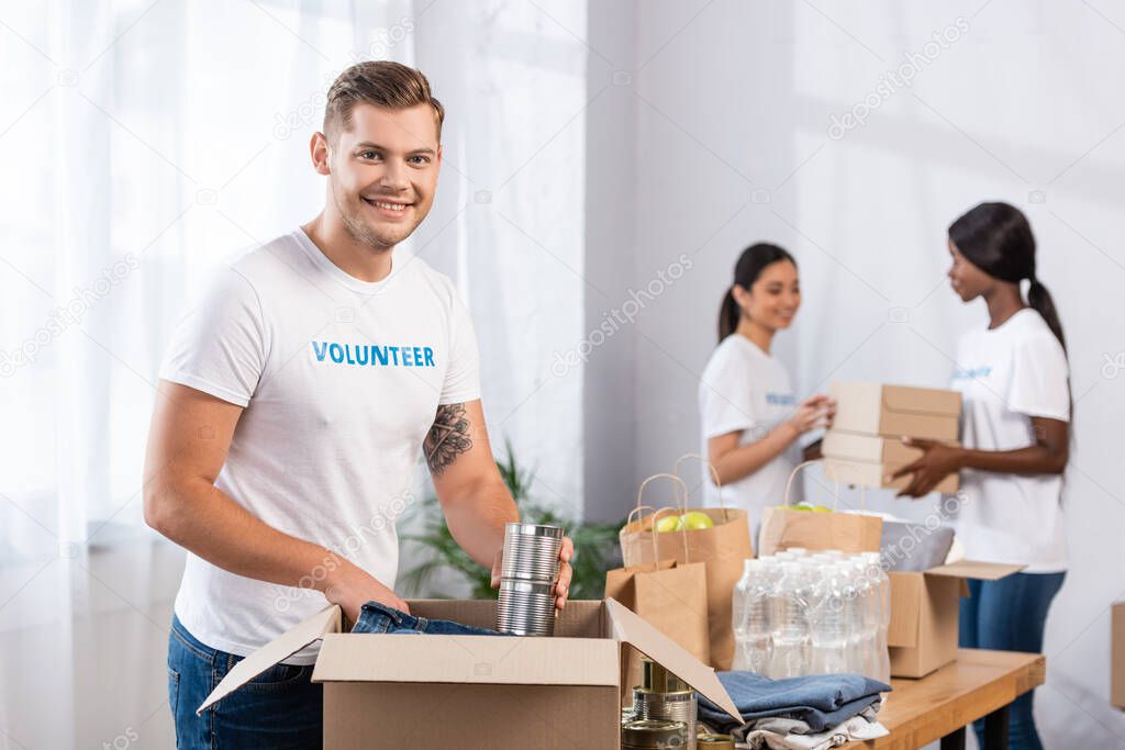 Selective focus of volunteer putting tin cans in carton box in charity center  