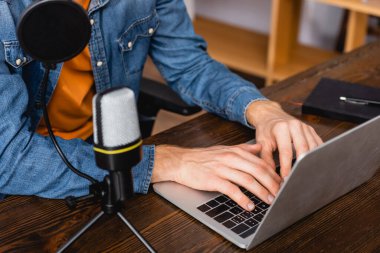 cropped view of broadcaster in denim shirt typing on laptop near microphone clipart