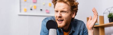 panoramic concept of worried redhead radio host speaking and gesturing near microphone clipart