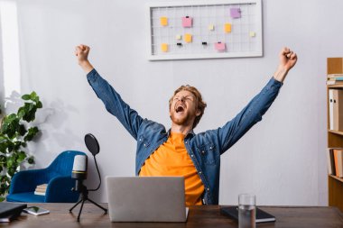 excited radio host showing triumph gesture while screaming near microphone and laptop clipart