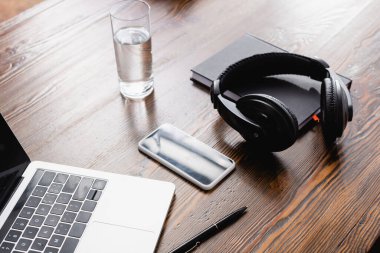 Kablosuz kulaklık, akıllı telefon, dizüstü bilgisayar, defter ve bir bardak su.