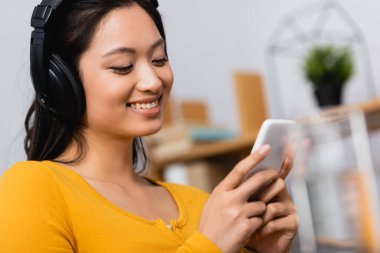 Asyalı esmer bir kadının kablosuz kulaklıkla podcast dinlerken akıllı telefon kullandığı seçici odak noktası.