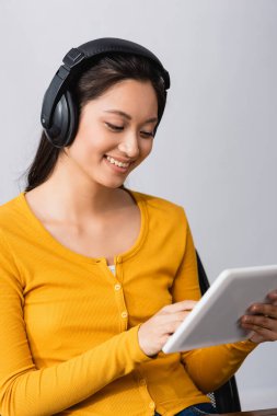 selective focus of young asian student listening podcast in wireless headphones while using digital tablet clipart