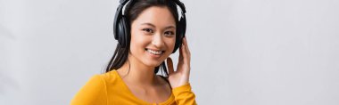 horizontal image of brunette asian woman touching wireless headphones while looking at camera clipart