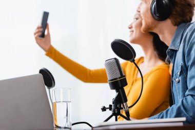 Asyalı spikerin iş yerindeki meslektaşıyla akıllı telefondan selfie çektiği seçici odak noktası.