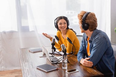 Telsiz kulaklıklı Asyalı spiker radyo stüdyosundaki meslektaşıyla konuşurken el kol hareketi yapıyor.