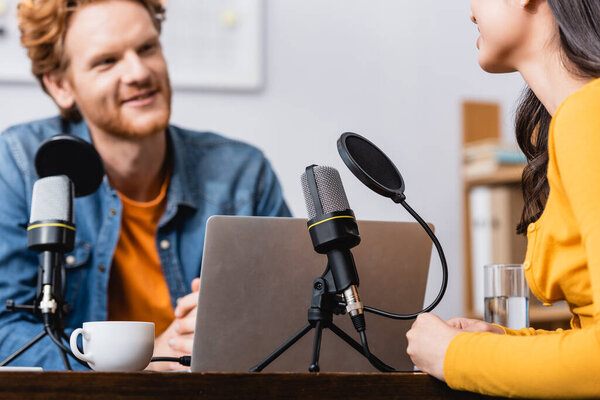 cropped view of young woman near microphone and broadcaster in radio studio