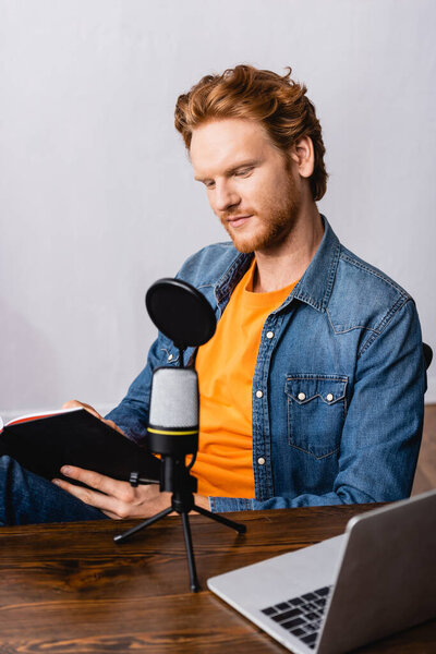 redhead broadcaster in denim shirt writing in notebook near microphone