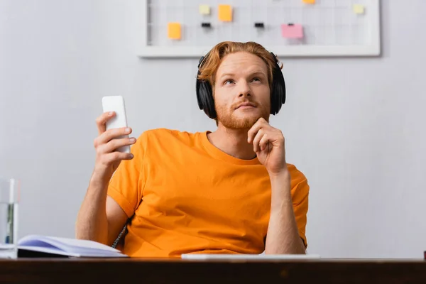 Dreamy Redhead Man Wireless Headphones Looking While Holding Smartphone — Stock Photo, Image