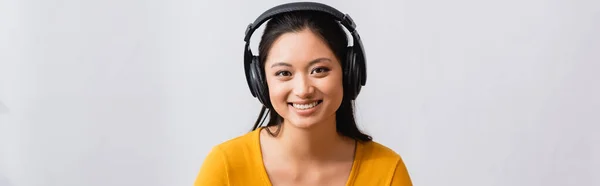 ブルネットのアジアの女性のウェブサイトヘッダーは ワイヤレスヘッドフォンでポッドキャストを聞いて カメラを見て — ストック写真