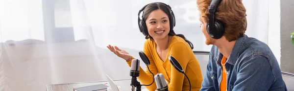 stock image horizontal image of asian announcer in wireless headphones gesturing while talking to colleague in studio