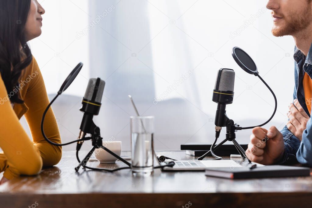 partial view of young woman and interviewer near microphones in radio studio