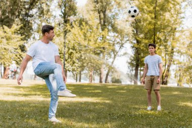 Genç oğlanla parkta futbol oynayan adamın seçici odak noktası.