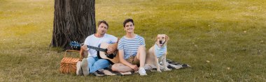 Genç çocuk ve babanın panoramik mahsulü Golden Retriever yakınlarında ağaç gövdesinin altında battaniyede oturuyorlar. 