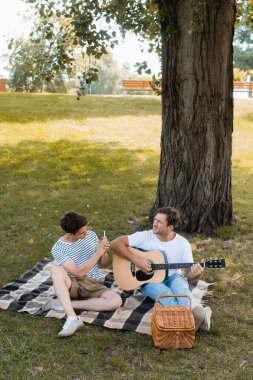 Genç çocuk babasının battaniyeye oturup akustik gitar çalarken fotoğrafını çekiyor. 