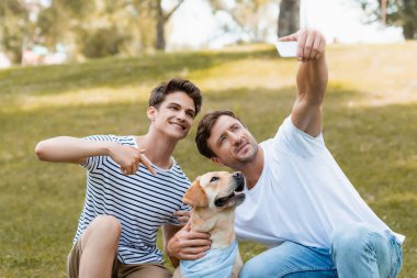 Baba selfie çekerken genç çocuk Golden Retriever 'ı işaret ediyor.
