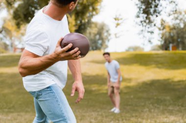 selective focus of man throwing rugby ball to son in park  clipart