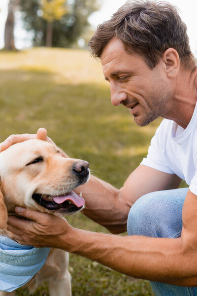 man in white t-shirt cuddling golden retriever in park 