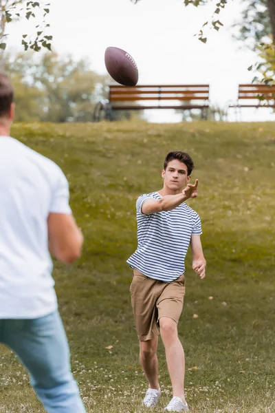 10代の少年がグリーンパークで父親にラグビーボールを投げ — ストック写真