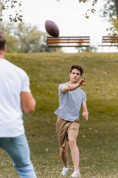 селективное внимание мальчика-подростка, бросающего мяч для регби отцу в зеленом парке 
